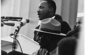 Dr. Martin Luther King, Jr. stands at a microphone giving a speech to a crowd.