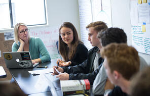 Students and teacher engage in discussion in a classroom. 