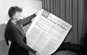 A black and white photo of Eleanor Roosevelt holding a large copy of the Universal Declaration of Human Rights in Spanish.