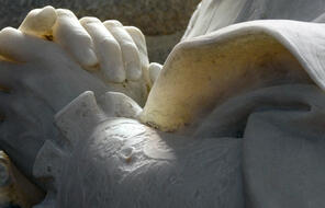 A close up of a marble statue with hands clasped together.