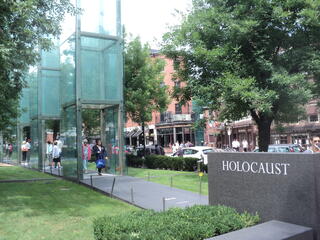 A stone sign on the right reads Holocaust, with three glass pillars in view at the New England Holocaust Memorial in Boston, MA.