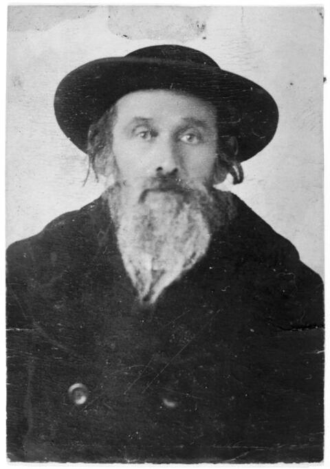 Portrait of a man with a long, grey, beard, and wearing a black hat and black clothes