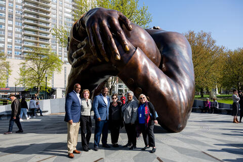 Five people stand in front of the Embrace, a memorial in Boston, MA.