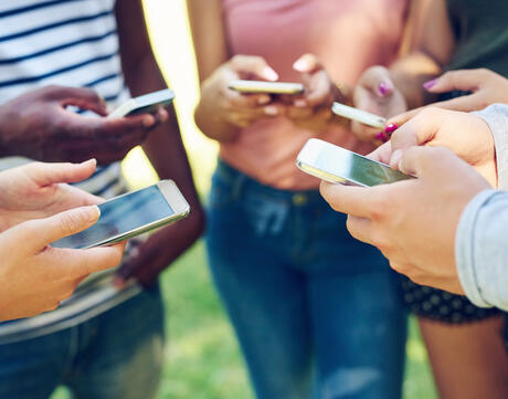 Cropped shot of a group of friends using their phones together outdoors